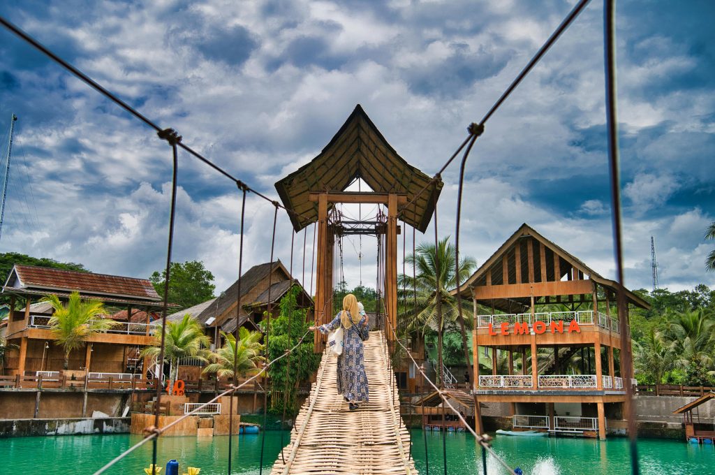 Woman walking on a wooden bridge at a tropical resort under a dramatic sky.