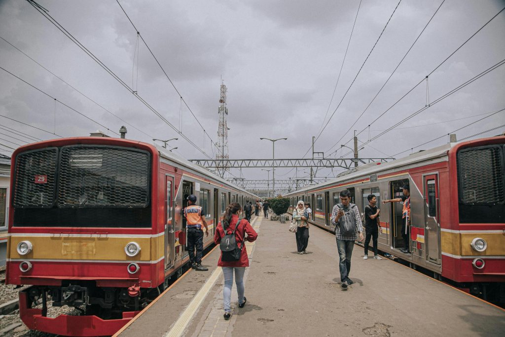 A bustling train station scene with people walking between trains on a cloudy day.
